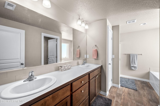 bathroom with vanity, hardwood / wood-style floors, a textured ceiling, and a tub to relax in