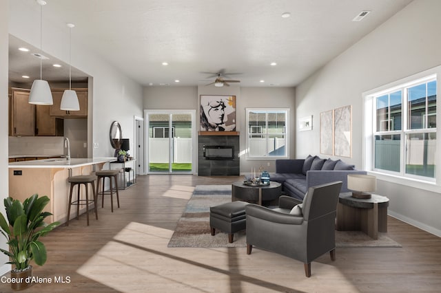 living room featuring ceiling fan, a tiled fireplace, sink, and hardwood / wood-style floors