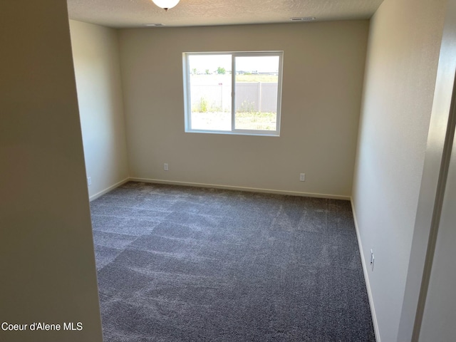 spare room featuring a textured ceiling, dark colored carpet, visible vents, and baseboards