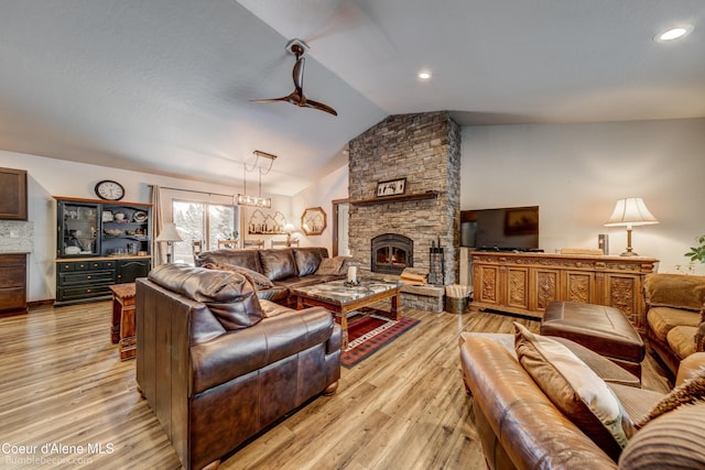 living room with a stone fireplace, vaulted ceiling, ceiling fan, and light wood-type flooring