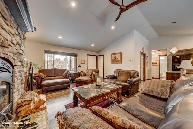 living room with ceiling fan, lofted ceiling, a stone fireplace, and light hardwood / wood-style flooring