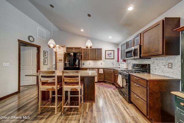 kitchen with decorative light fixtures, lofted ceiling, a kitchen breakfast bar, a center island, and black appliances