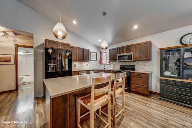 kitchen featuring decorative light fixtures, vaulted ceiling, a kitchen breakfast bar, a kitchen island, and black appliances