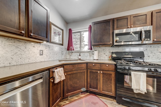 kitchen with sink, stainless steel appliances, tasteful backsplash, dark brown cabinetry, and light hardwood / wood-style floors