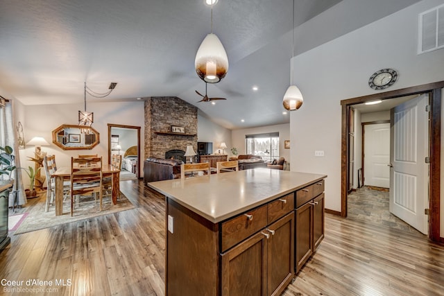 kitchen with lofted ceiling, a stone fireplace, decorative light fixtures, light wood-type flooring, and a kitchen island