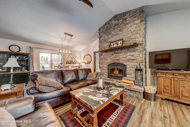 living room with vaulted ceiling, a stone fireplace, an inviting chandelier, and light hardwood / wood-style flooring