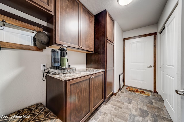 kitchen featuring light stone counters, dark brown cabinetry, and a textured ceiling