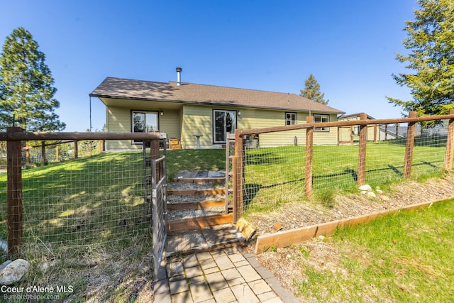 rear view of property featuring fence, a yard, and roof with shingles