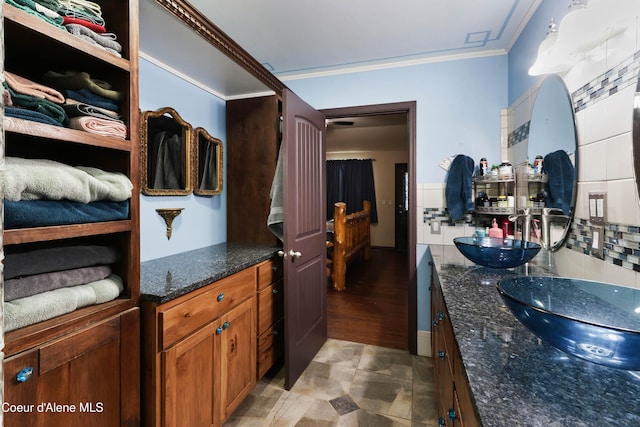 kitchen featuring tasteful backsplash, sink, ornamental molding, and dark stone countertops