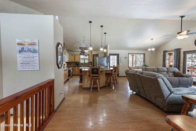 living room with vaulted ceiling, ceiling fan with notable chandelier, and light hardwood / wood-style flooring