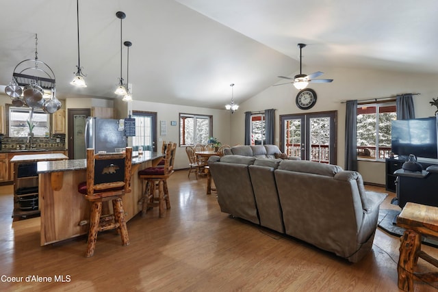 living room with ceiling fan with notable chandelier, high vaulted ceiling, sink, light wood-type flooring, and french doors