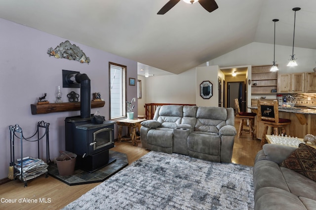 living room with ceiling fan, light wood-type flooring, vaulted ceiling, and a wood stove