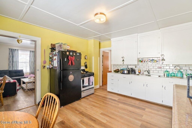 kitchen with black refrigerator, stainless steel gas stove, sink, white cabinets, and light hardwood / wood-style floors