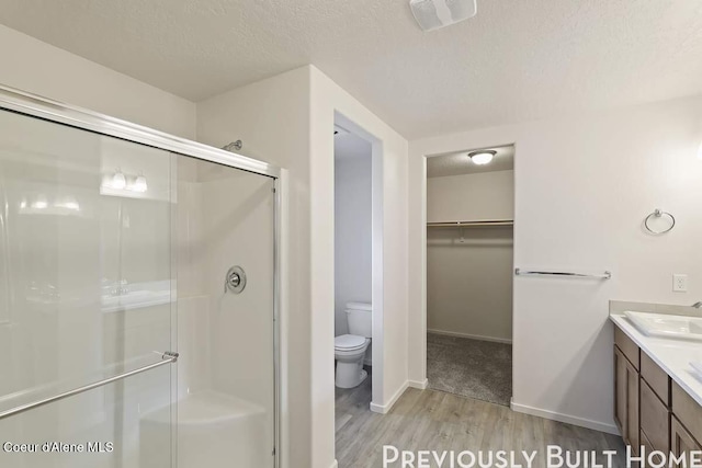 full bathroom featuring a shower stall, a walk in closet, a textured ceiling, and wood finished floors