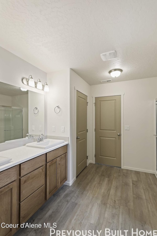 bathroom with wood finished floors, visible vents, a textured ceiling, a shower stall, and vanity