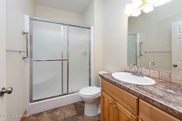 bathroom featuring toilet, a shower stall, stone finish flooring, and vanity