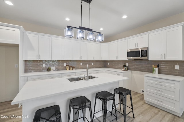 kitchen featuring sink, white cabinetry, hanging light fixtures, a kitchen island with sink, and light hardwood / wood-style floors