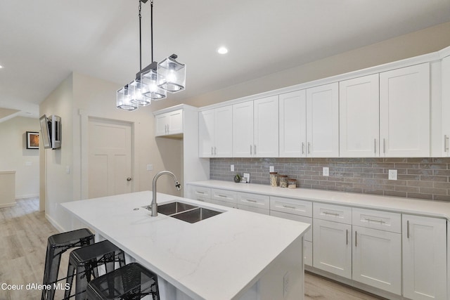 kitchen with a kitchen island with sink, sink, hanging light fixtures, and white cabinets