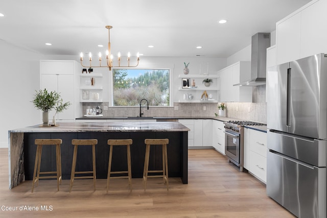 kitchen with white cabinetry, appliances with stainless steel finishes, pendant lighting, dark stone counters, and wall chimney range hood