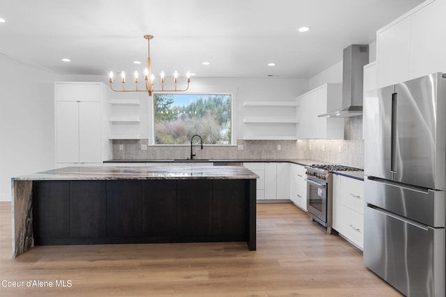 kitchen with a kitchen island, appliances with stainless steel finishes, white cabinets, hanging light fixtures, and wall chimney exhaust hood