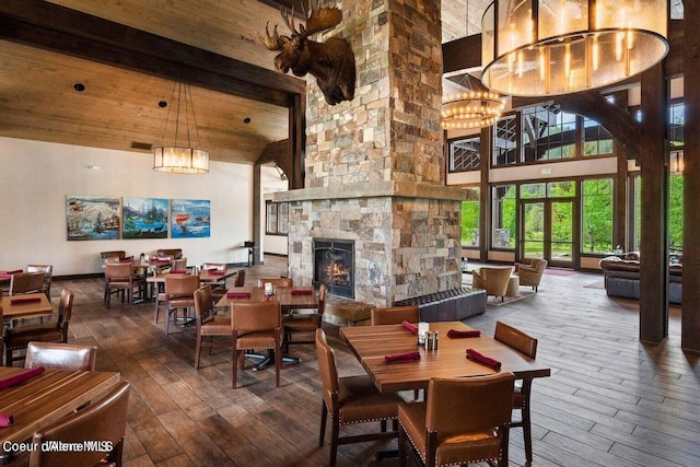 dining area featuring wood ceiling, an inviting chandelier, high vaulted ceiling, wood-type flooring, and a stone fireplace