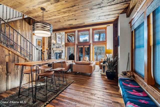 dining area with hardwood / wood-style floors, a stone fireplace, a towering ceiling, wooden ceiling, and wooden walls