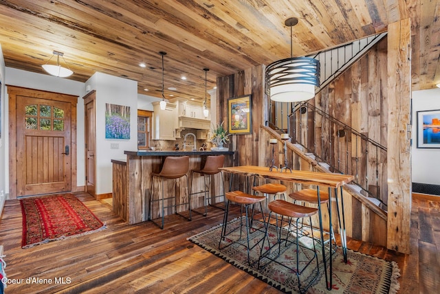 dining room featuring dark hardwood / wood-style flooring, sink, wood ceiling, and wooden walls
