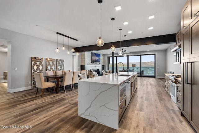 kitchen featuring dark brown cabinetry, sink, light stone counters, decorative light fixtures, and a large island with sink