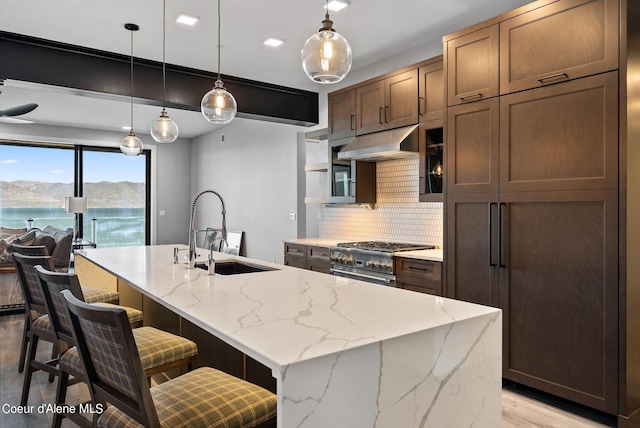 kitchen with pendant lighting, sink, high end range, light stone counters, and a center island with sink