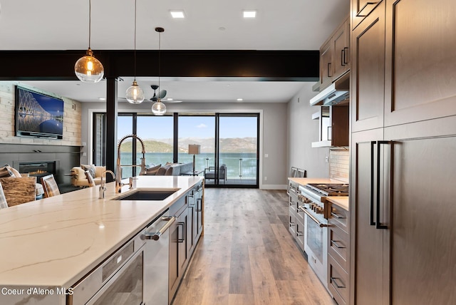 kitchen with a fireplace, decorative light fixtures, beamed ceiling, sink, and light stone counters