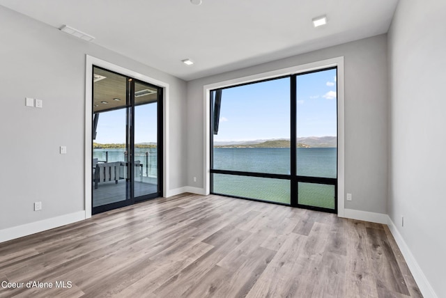 unfurnished room featuring a water view and light hardwood / wood-style floors