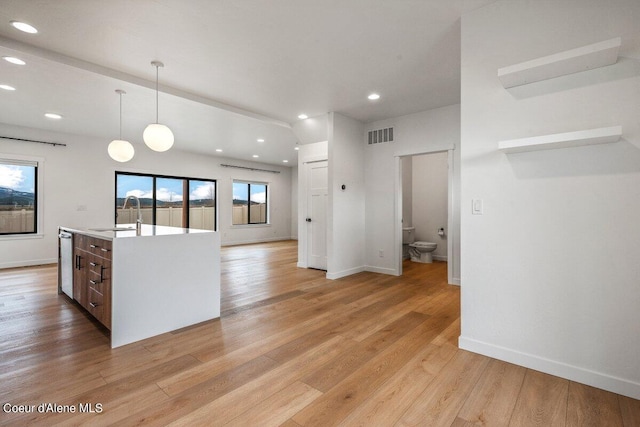 kitchen with decorative light fixtures, sink, a center island with sink, and light hardwood / wood-style flooring