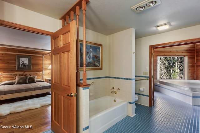 bathroom featuring a bathtub, a textured ceiling, tile patterned floors, toilet, and wood walls