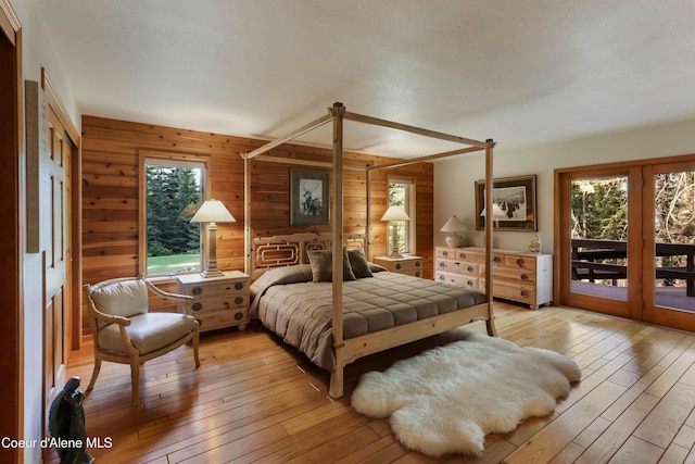 bedroom with access to outside, light hardwood / wood-style floors, and wood walls