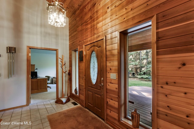 entryway featuring a notable chandelier, a towering ceiling, wooden walls, and light tile patterned flooring