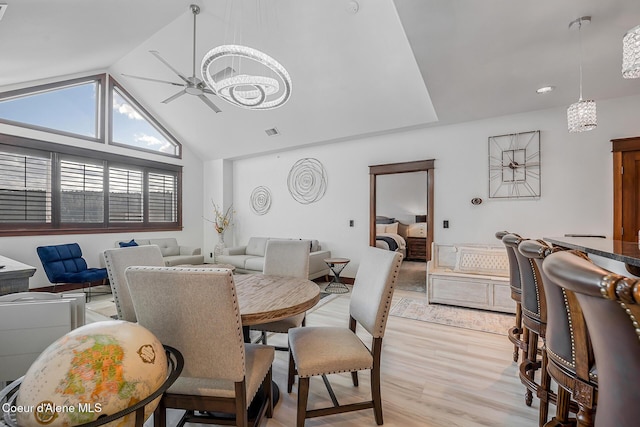 dining area with high vaulted ceiling, ceiling fan with notable chandelier, and light hardwood / wood-style floors