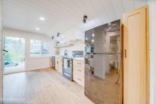 kitchen featuring premium range hood, vaulted ceiling, sink, stainless steel appliances, and light hardwood / wood-style flooring