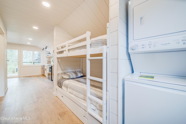 bedroom with stacked washer and dryer, vaulted ceiling, and light wood-type flooring