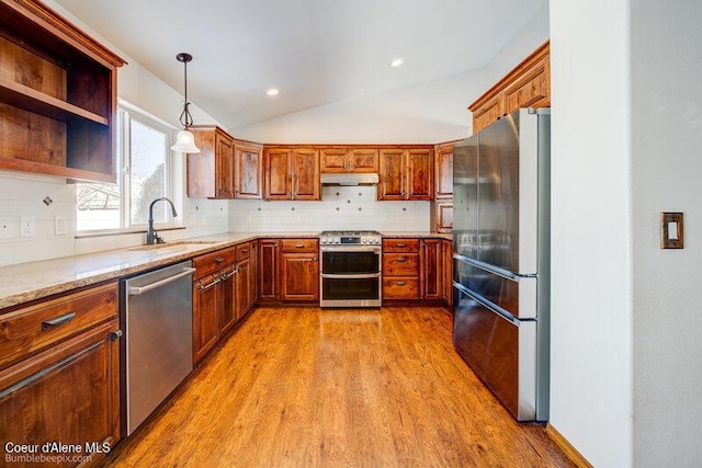 kitchen featuring sink, vaulted ceiling, pendant lighting, stainless steel appliances, and light stone countertops