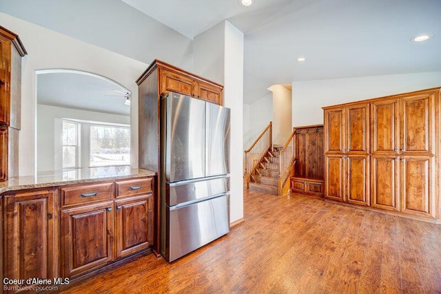 kitchen with stainless steel refrigerator, lofted ceiling, light stone counters, and light hardwood / wood-style flooring