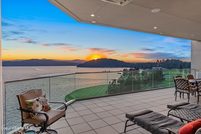 patio terrace at dusk with a water and mountain view and a balcony