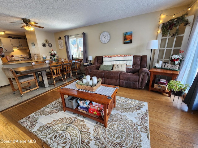 living room with ceiling fan, a textured ceiling, and light hardwood / wood-style flooring