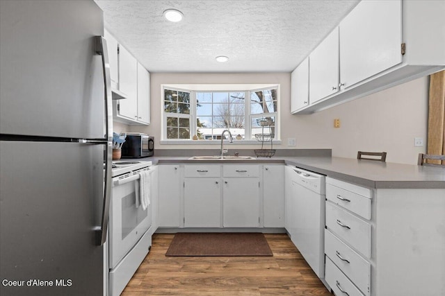 kitchen with white appliances, wood finished floors, a textured ceiling, white cabinetry, and a sink