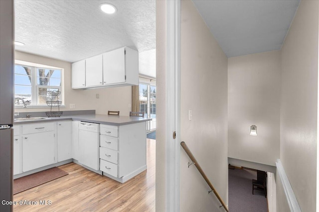 kitchen with light wood finished floors, white cabinets, dishwasher, light countertops, and a sink