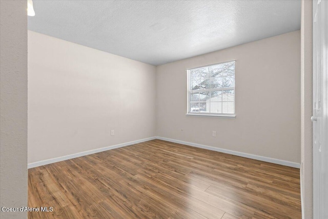 empty room with a textured ceiling, baseboards, and wood finished floors