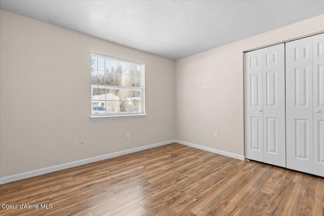 unfurnished bedroom featuring a textured ceiling, a closet, wood finished floors, and baseboards