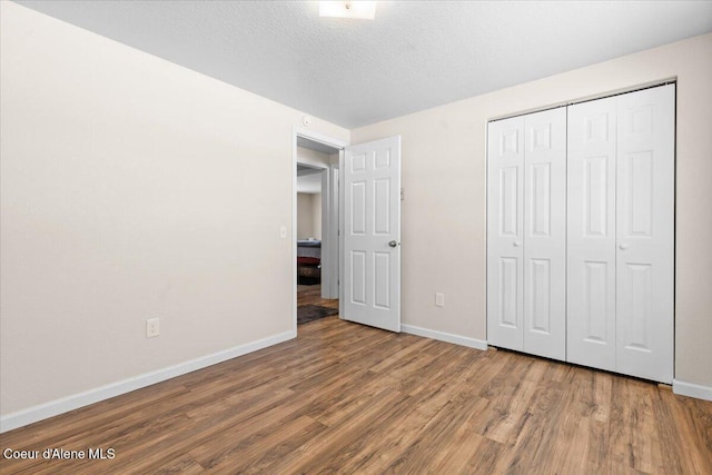 unfurnished bedroom featuring a closet, a textured ceiling, baseboards, and wood finished floors