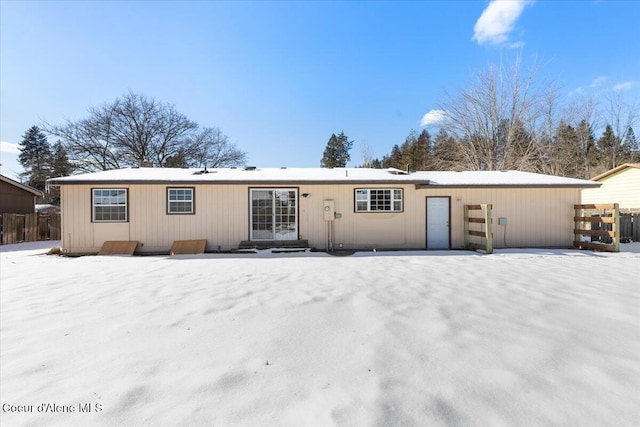 snow covered rear of property featuring entry steps and fence