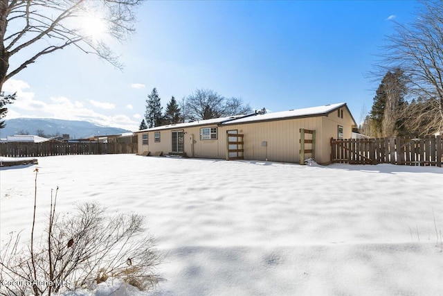 snow covered back of property with a mountain view and fence