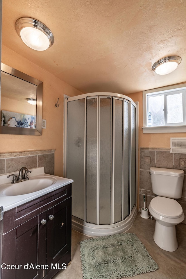 bathroom featuring tile walls, vanity, a shower with shower door, and toilet